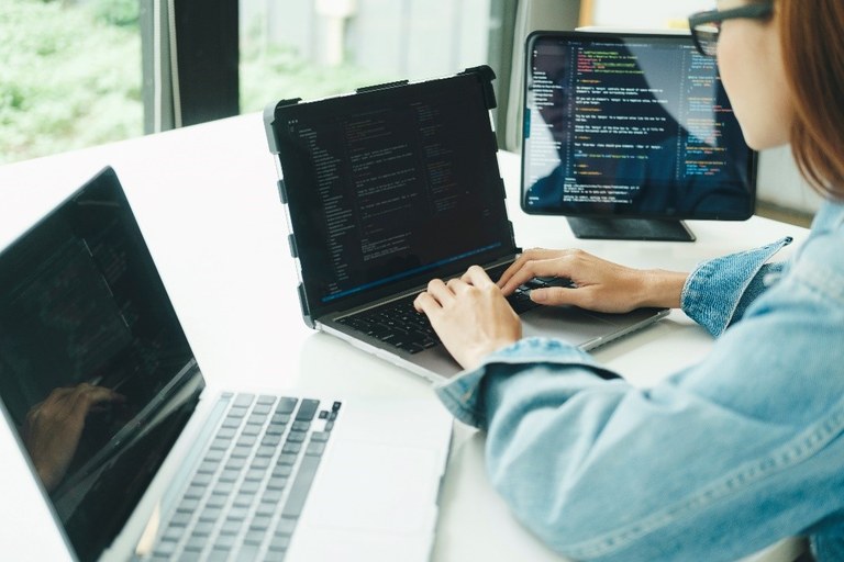 Junge Frau arbeitet an einem Laptop. Auf dem Bildschirm sieht man einen Programmcode. 