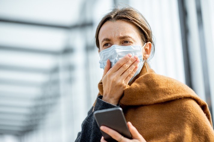 Junge, besorgte Frau mit Gesichtsmaske, liest schlechte Nachrichten auf einem Smartphone an einer Haltestelle .